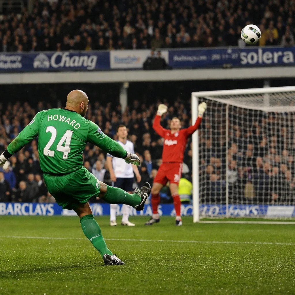 A wide football pitch showing a goalkeeper delivering a long kick from inside his penalty area while the opposing goalkeeper stands near the far goal; cloudy sky and stadium stands in the background.